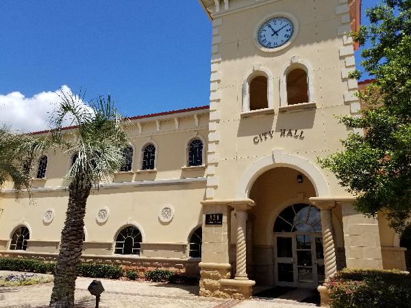 Front of Green Cove City Hall during the day with a blue sky and a cloud in the background and palm trees out front.